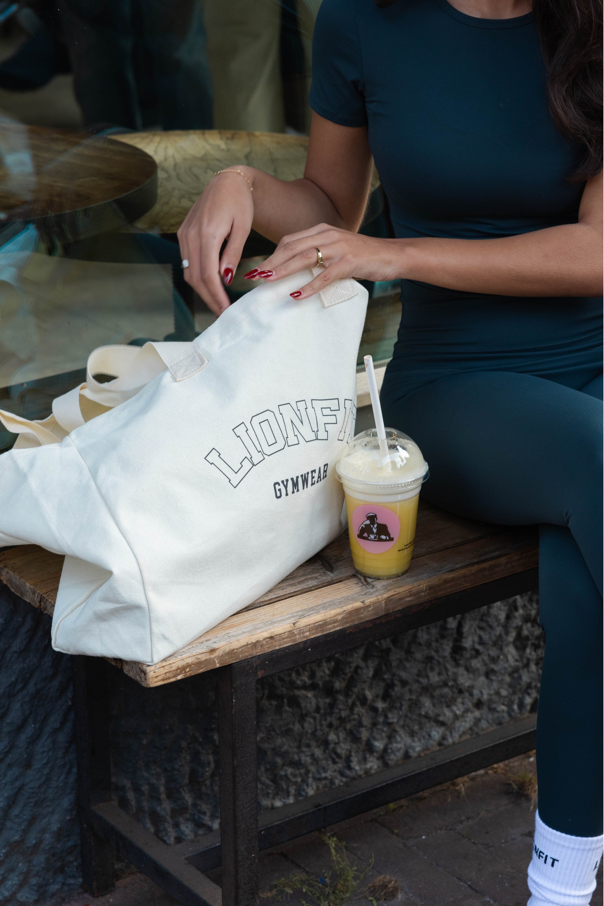 Vrouw met de Essential Totebag Beige van Lionfit Gymwear in sportieve outfit, buiten bij daglicht. Grote katoenen shopper tas perfect voor sportschool, strand of dagelijks gebruik, gemaakt van duurzaam gerecycled materiaal.