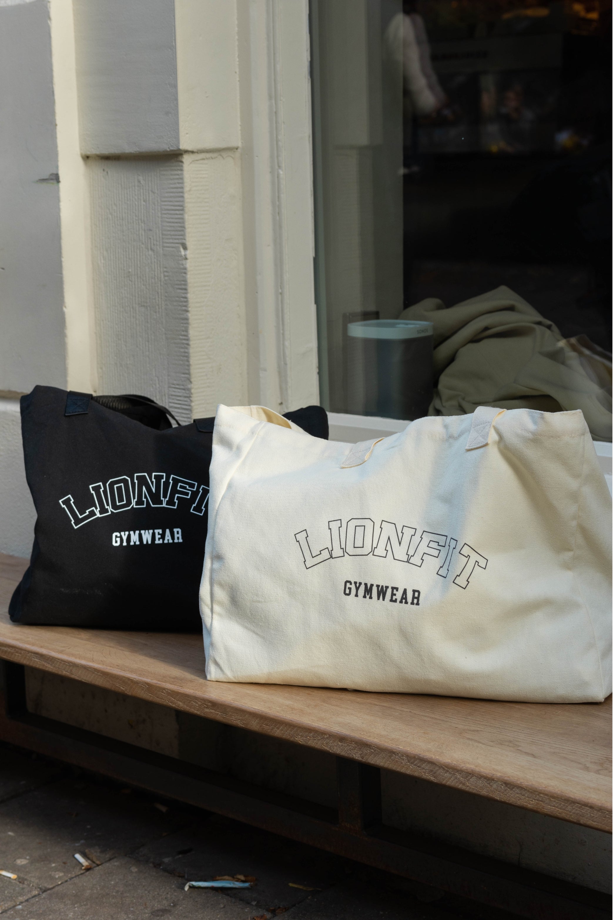 Vrouw met de Essential Totebag Beige van Lionfit Gymwear in sportieve outfit, buiten bij daglicht. Grote katoenen shopper tas perfect voor sportschool, strand of dagelijks gebruik, gemaakt van duurzaam gerecycled materiaal.