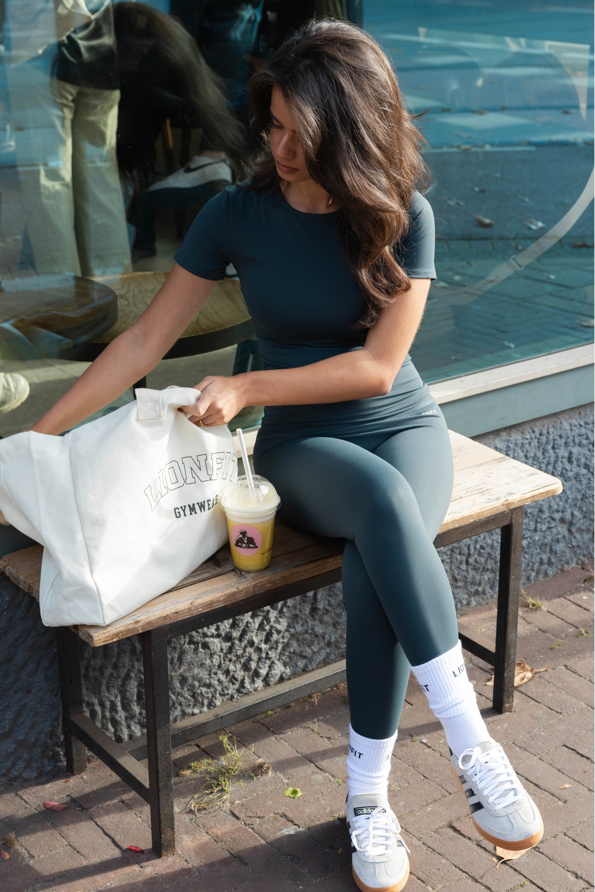 Vrouw met de Essential Totebag Beige van Lionfit Gymwear in sportieve outfit, buiten bij daglicht. Grote katoenen shopper tas perfect voor sportschool, strand of dagelijks gebruik, gemaakt van duurzaam gerecycled materiaal.