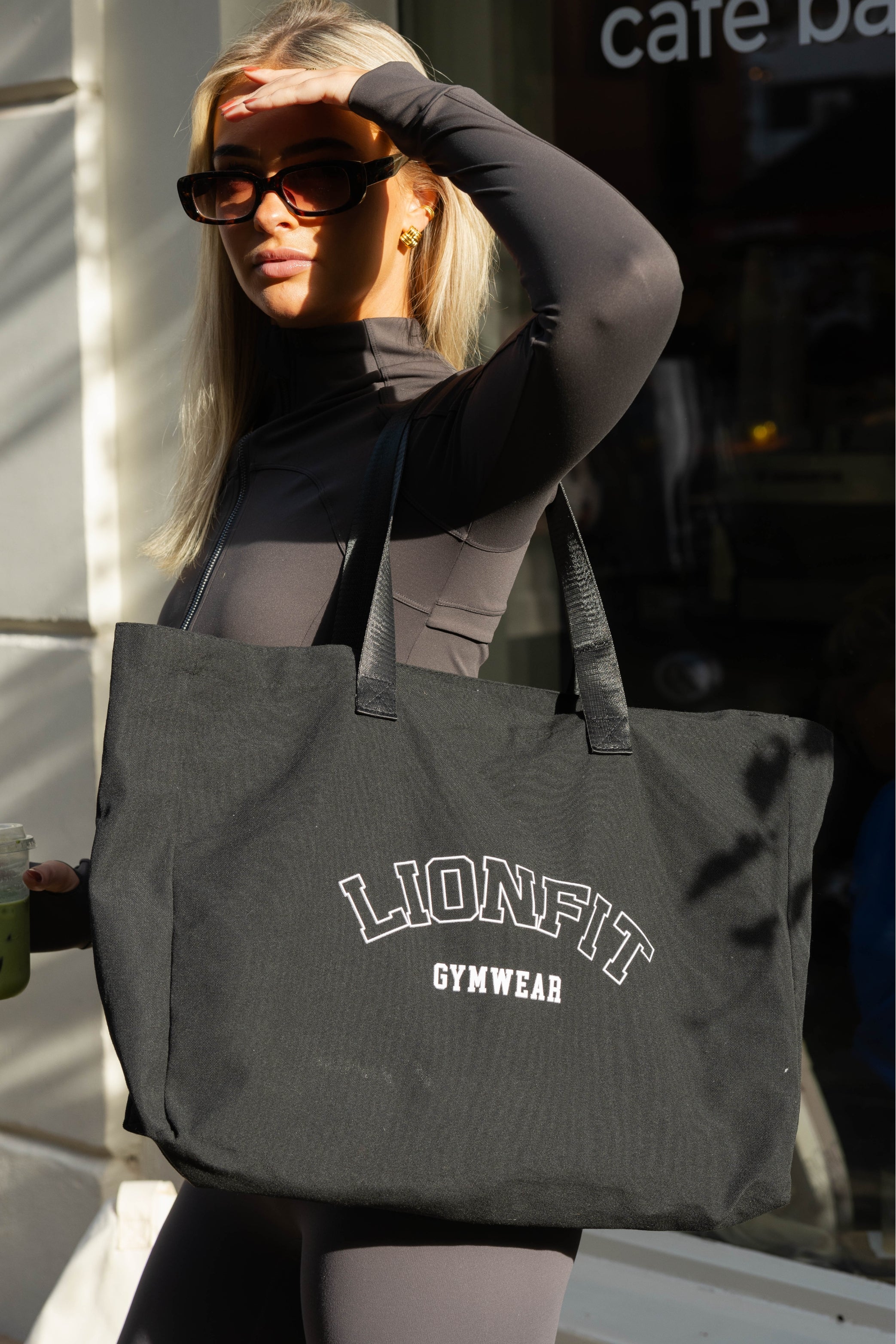 Vrouw met de zwarte Essential Totebag van Lionfit Gymwear, een grote katoenen shopper ideaal voor sportschool, dagelijks gebruik en strand. Gemaakt van gerecycled materiaal, biedt deze duurzame tas een stijlvolle en praktische oplossing voor actieve vrouwen.