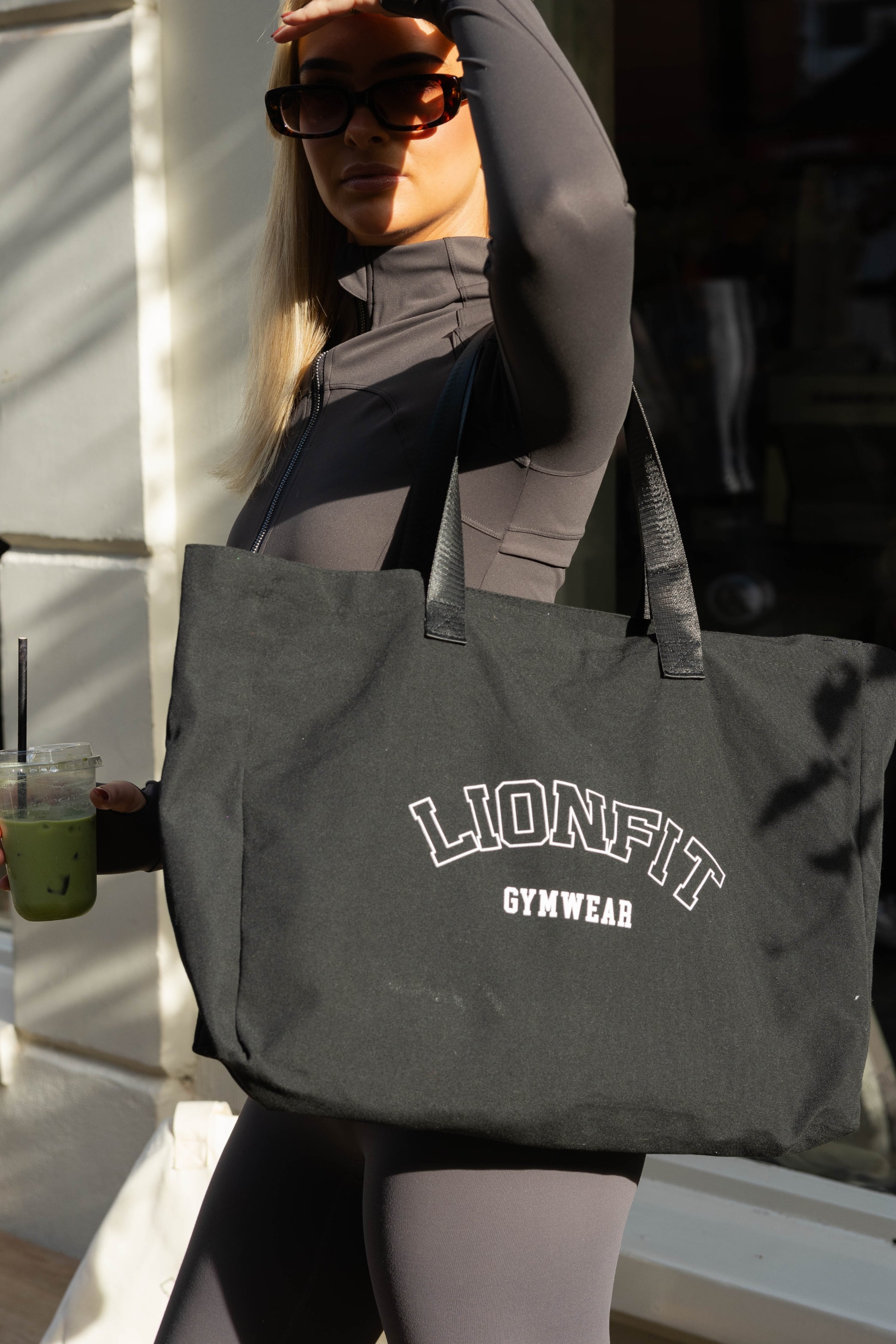 Vrouw met de zwarte Essential Totebag van Lionfit Gymwear, een grote katoenen shopper ideaal voor sportschool, dagelijks gebruik en strand. Gemaakt van gerecycled materiaal, biedt deze duurzame tas een stijlvolle en praktische oplossing voor actieve vrouwen.