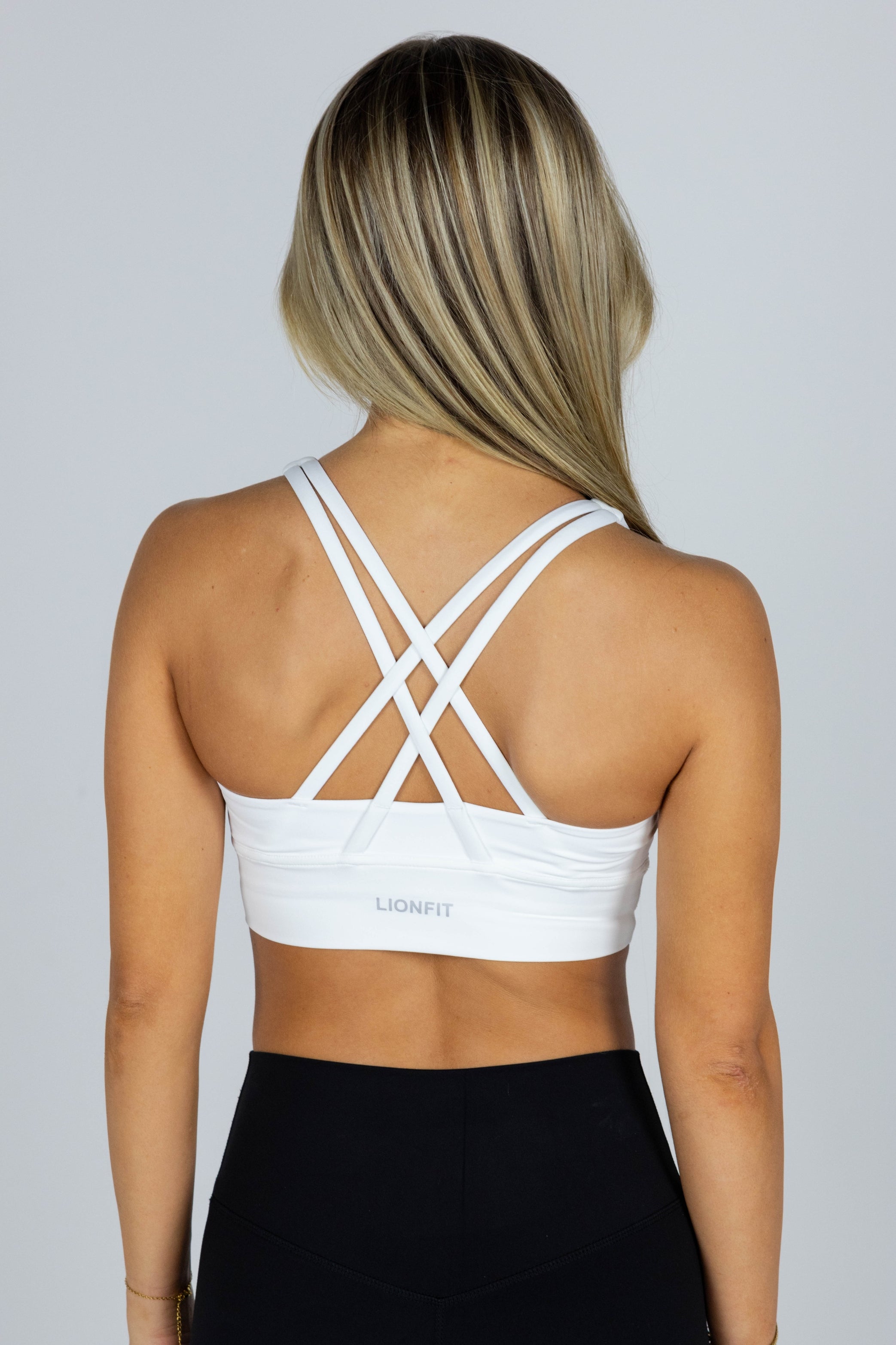 Vrouw draagt de Essential Seamless Cross Bra White van Lionfit – naadloze witte sport-bh met gekruiste bandjes, perfect voor yoga, fitness en alledaags comfort