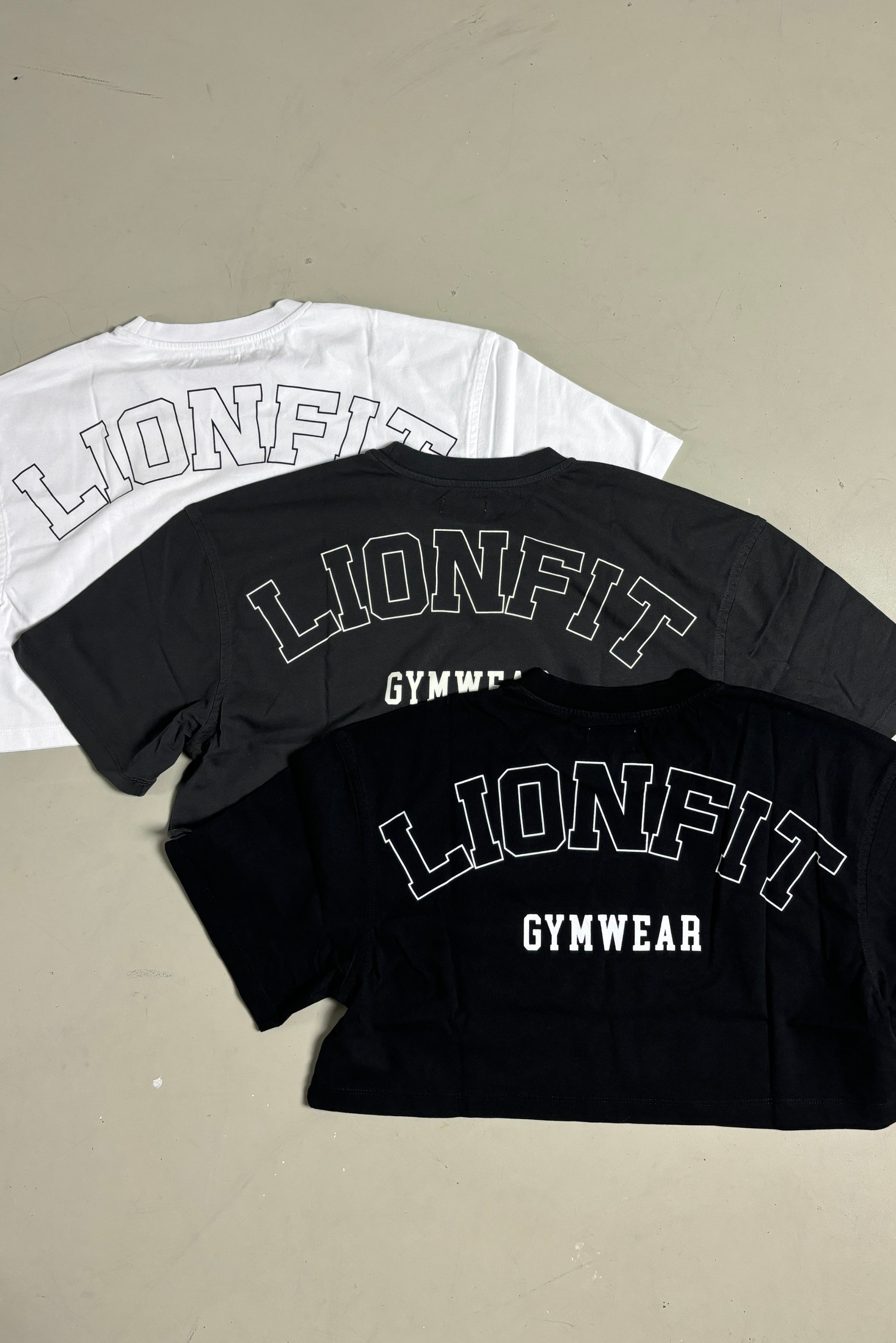 Dames cropped T-shirt van Lion Fit Gymwear in zwart, wit en grijs, met grote rugprint "LIONFIT GYMWEAR". Ideaal voor sport en casual dragen.